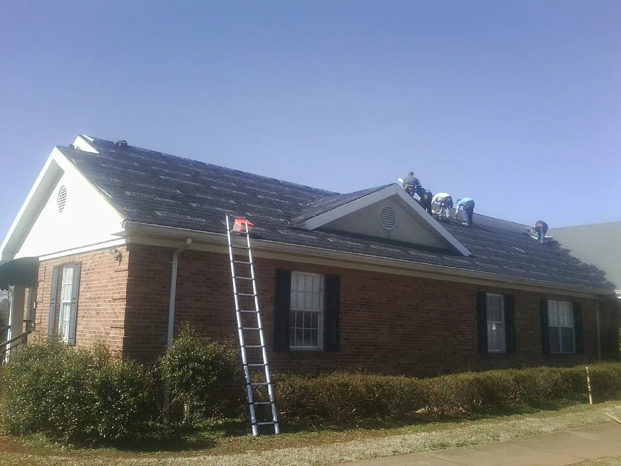 Crew tearing shingles off a brick ranch roof with a ladder set — Metal Roof Repair work by our crew in Lake Elsinore