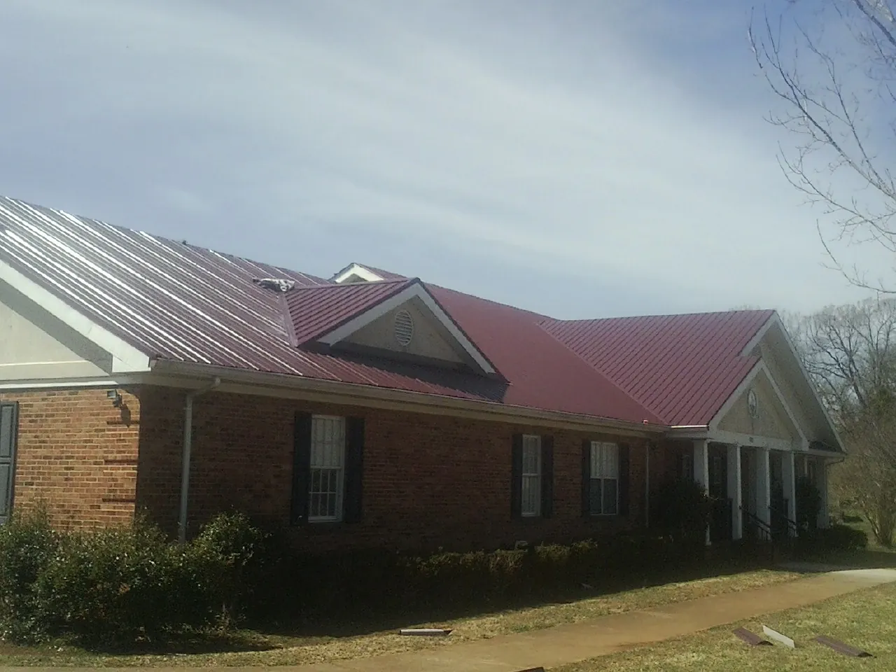 Red metal roof with gabled entries on a long brick building, from a Hail Damage Roof Repair job in Lake Elsinore