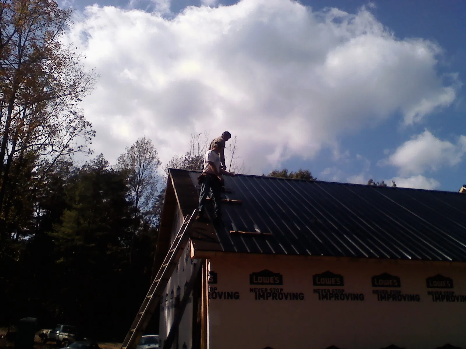 Roofer fastening dark metal panels high against a cloudy sky, from a Roof Inspection job in Lake Elsinore