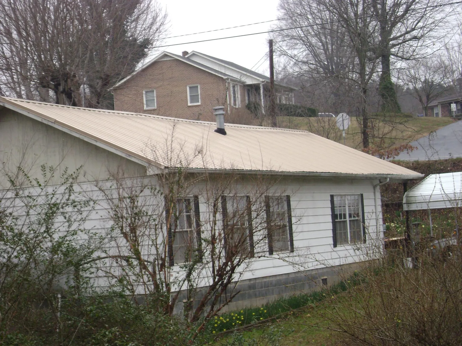 Tan metal roof on a white sided house set into a hillside — Commercial Roofing by Roofing Brothers in Lake Elsinore